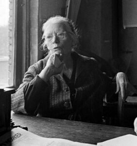 Dorothy Day, seated by city window, with hand propped upon chin