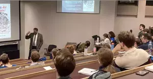 Man in suit delivers lecture to full room